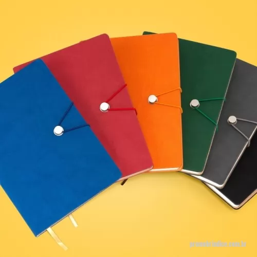Caderneta personalizada - Caderneta com fecho de pino e elástico de nylon para lacre. Capa em material sintético emborrachado, possui aproximadamente 96 folhas pardas pautadas e marca página em cetim.