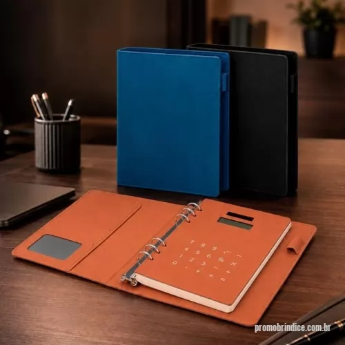 Caderno Capa Dura personalizado - Caderno tipo fichário com capa dura em poliuretano (PU). Possui seis argolas metálicas, aba interna com compartimento para três cartões e visor plástico transparente para documento, suporte lateral para caneta e calculadora alimentada por energia solar com teclas touch e estrutura em PU. Apresenta cerca de 96 folhas tamanho A5 marfim pautadas de 75 g/m².