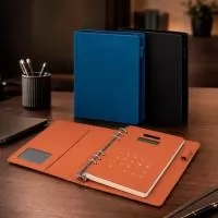 Caderno tipo fichário com capa dura em poliuretano (PU). Possui seis argolas metálicas, aba interna com compartimento para três cartões e visor plástico transparente para documento, suporte lateral para caneta e calculadora alimentada por energia solar com teclas touch e estrutura em PU. Apresenta cerca de 96 folhas tamanho A5 marfim pautadas de 75 g/m².