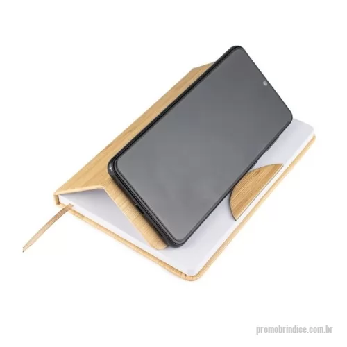 Caderno ecológico personalizado - A caderneta feita para quem valoriza praticidade com um toque de estilo. Feita em plástico, sua capa se assemelha ao charme natural do bambu, chamando a atenção em qualquer lugar. Internamente, o marcador de cetim facilita o acesso às anotações, que ganham vida em 80 páginas brancas pautadas, prontas para organizar suas ideias, listas e inspirações. O grande diferencial? O suporte para celular embutido na capa, perfeito para acompanhar vídeos, chamadas e até mesmo reuniões.