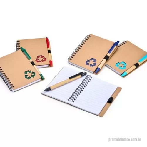 Caderno ecológico personalizado - Este caderno é uma ótima opção para fazer anotações sem abrir mão da sustentabilidade. Com capa produzida em papelão com detalhe vazado que remete ao símbolo da reciclagem, ele conta com encadernação Wire-O e aproximadamente 70 folhas brancas pautadas, trazendo muitas possibilidades para realizar todos os tipos de anotações durante um dia em movimento. O caderno acompanha uma caneta esferográfica de carga azul de 1,0 mm com corpo em papelão e clip, acionamento em clique e ponteira em plástico. A capa contém um elástico para abrigar a caneta junto ao caderno.