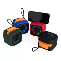 Caixa de som multimídia em plástico com espaço superior para encaixe do celular e base com revestimento antiderrapante. Oferece conectividade Bluetooth e entrada auxiliar P2, além de cartão TF (microSD) e USB-C, permitindo a reprodução de arquivos MP3. Acompanha cordão de nylon e cabo USB-C para carregamento.