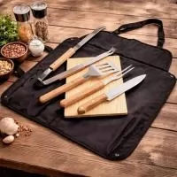 Descrição: Kit para churrasco composto por seis peças: avental em Oxford com fechamento em engate plástico, que pode ser dobrado e utilizado como estojo, com alças de mão e bolsos multiuso; tábua em madeira de pinho; e quatro utensílios em inox com cabos em madeira, incluindo garfo de duas pontas, espátula, pegador e faca com lâmina de 8 polegadas.